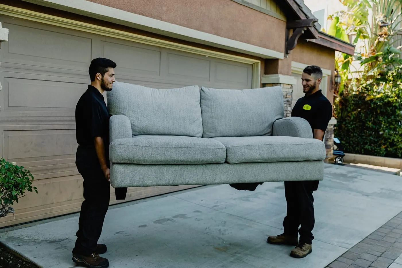 Two crew members carrying a couch out of a garage