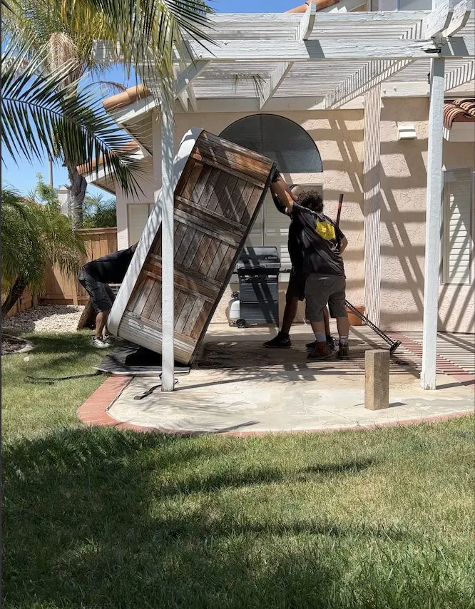 Crew moving a hot tub on its side out of a backyard