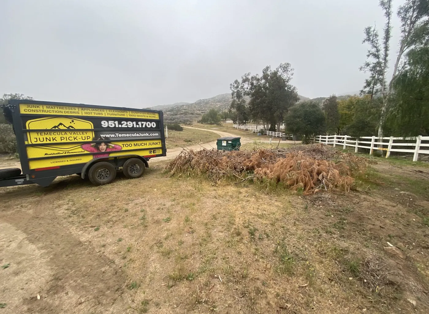 Dump trailer next to a pile of yard debris on a large lot
